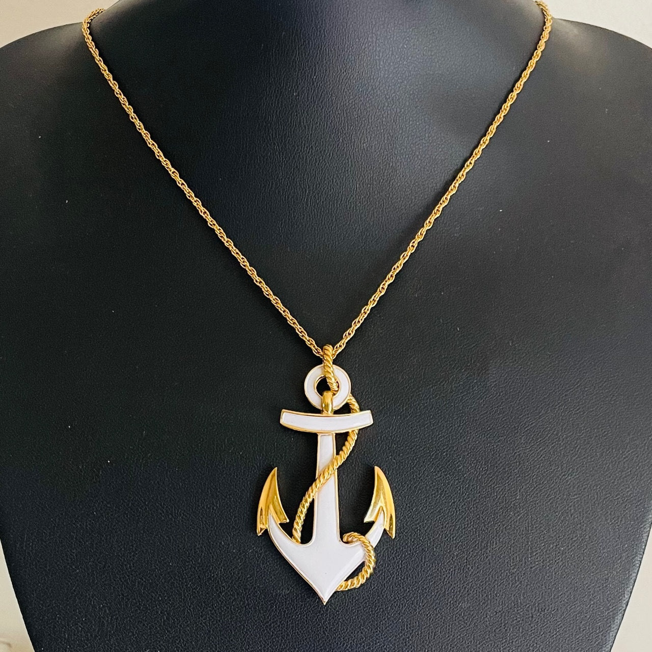 vintage mid-century Crown Trifari gold-tone anchor pendant necklace featuring a white enamel finish and an entwined textured marine rope accent shown on black bust
