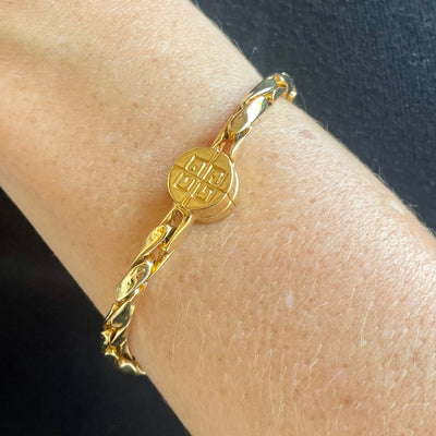 A close-up of a gold vintage bracelet worn on a person's wrist. Gold-tone vintage Givenchy chain bracelet from the 1980s, featuring polished interlocking links and a round magnetic clasp engraved with the iconic 4G logo.