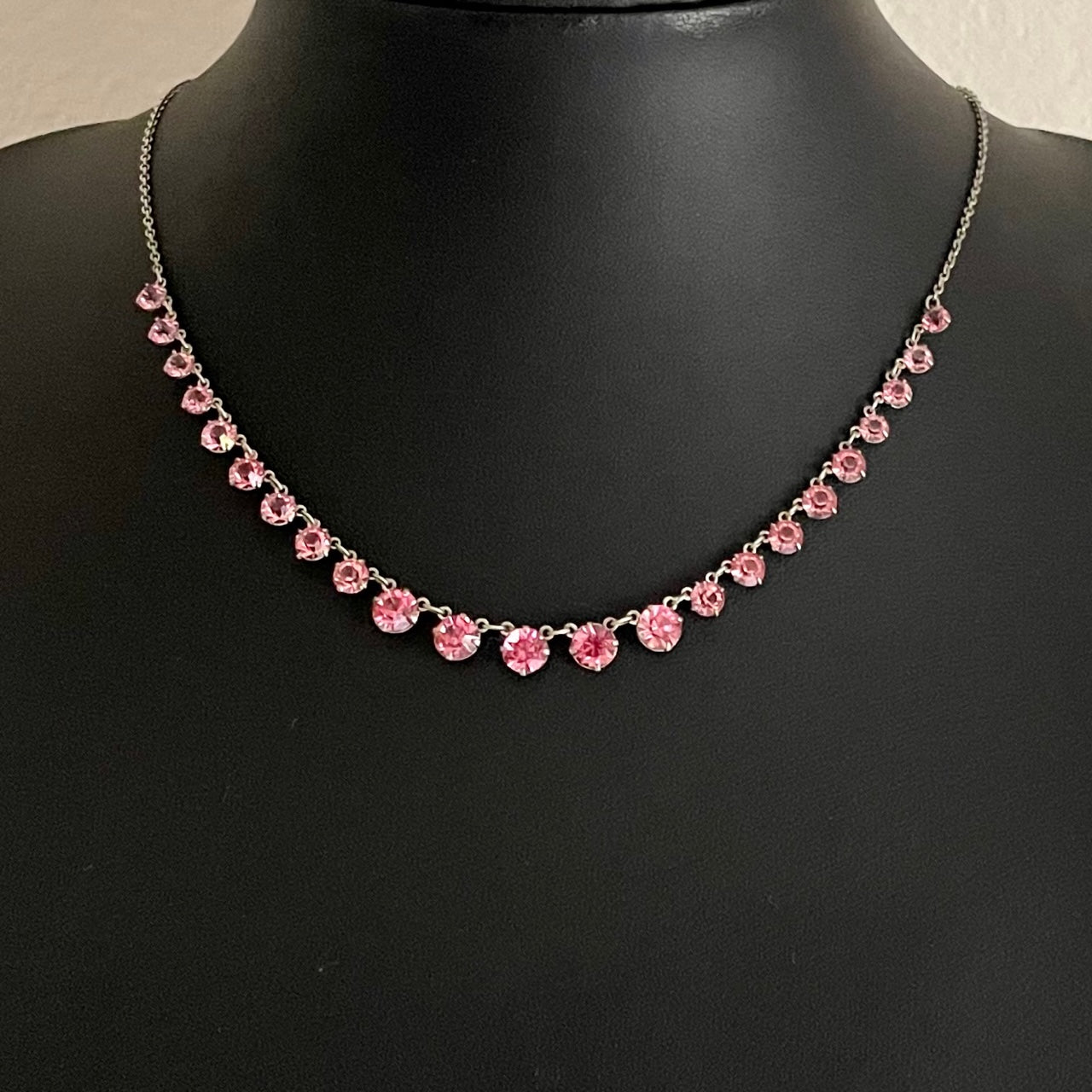 Art Deco blush pink glass rivière necklace with round-cut crystals in open-bezel settings on a delicate silver-tone chain, displayed on a black mannequin neck
