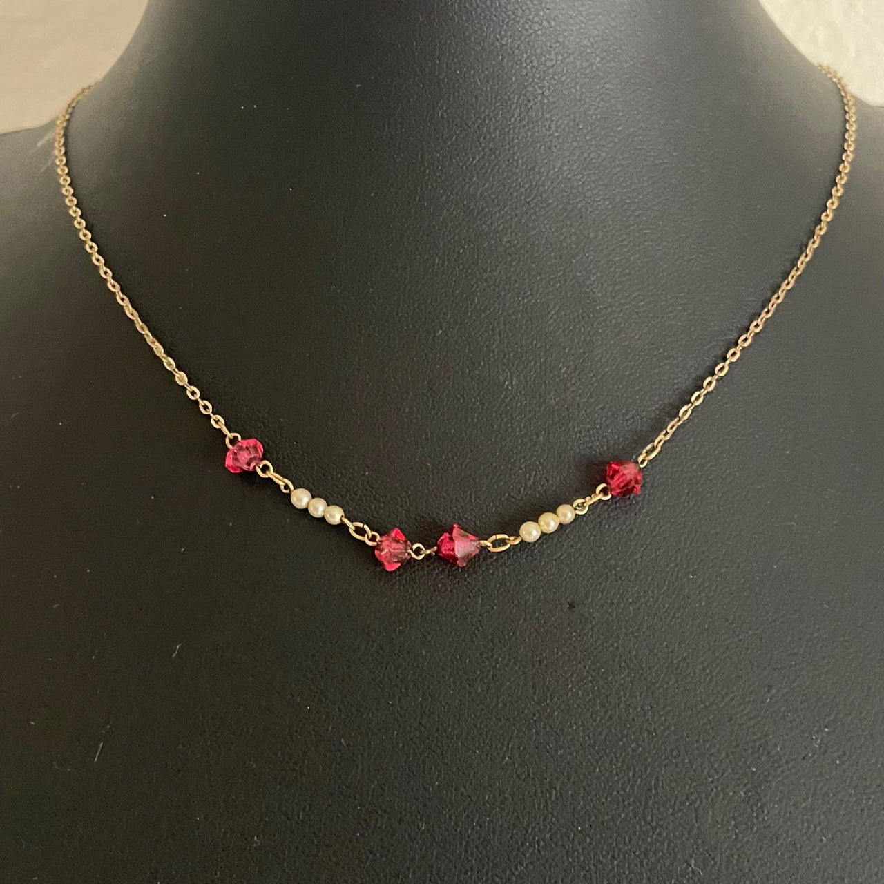 Art Deco necklace with geometric bicone-cut red crystals and tiny cream seed pearls spaced along a delicate gold-filled chain, displayed on a black mannequin.