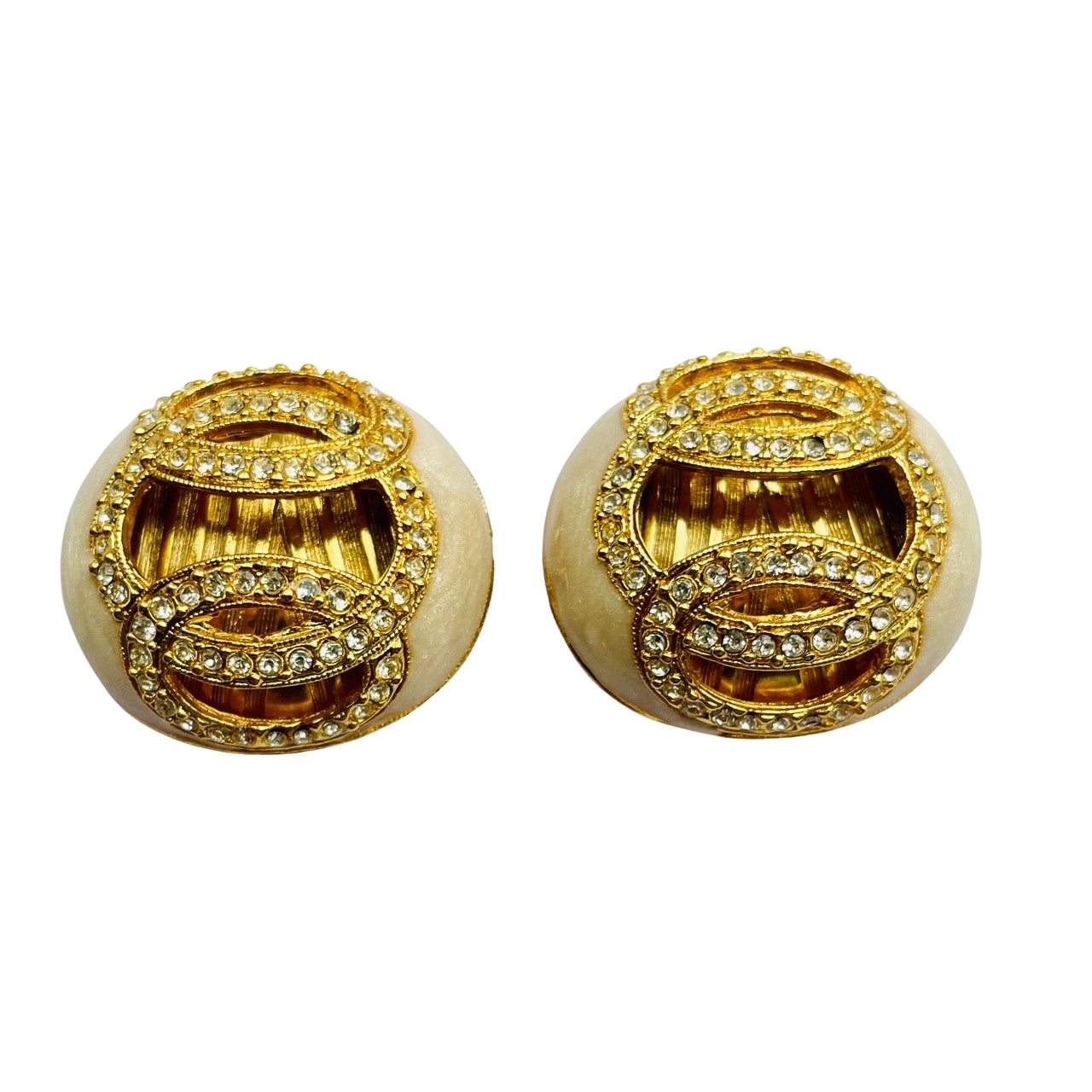 a pair of vintage 1980s Helena Rubinstein Paris domed clip-on earrings. Each button-style earring features a smooth, cream-colored faux pearl base overlaid with intricate gold-tone fluting and two interlocking circular motifs encrusted with small, glittering clear rhinestones.