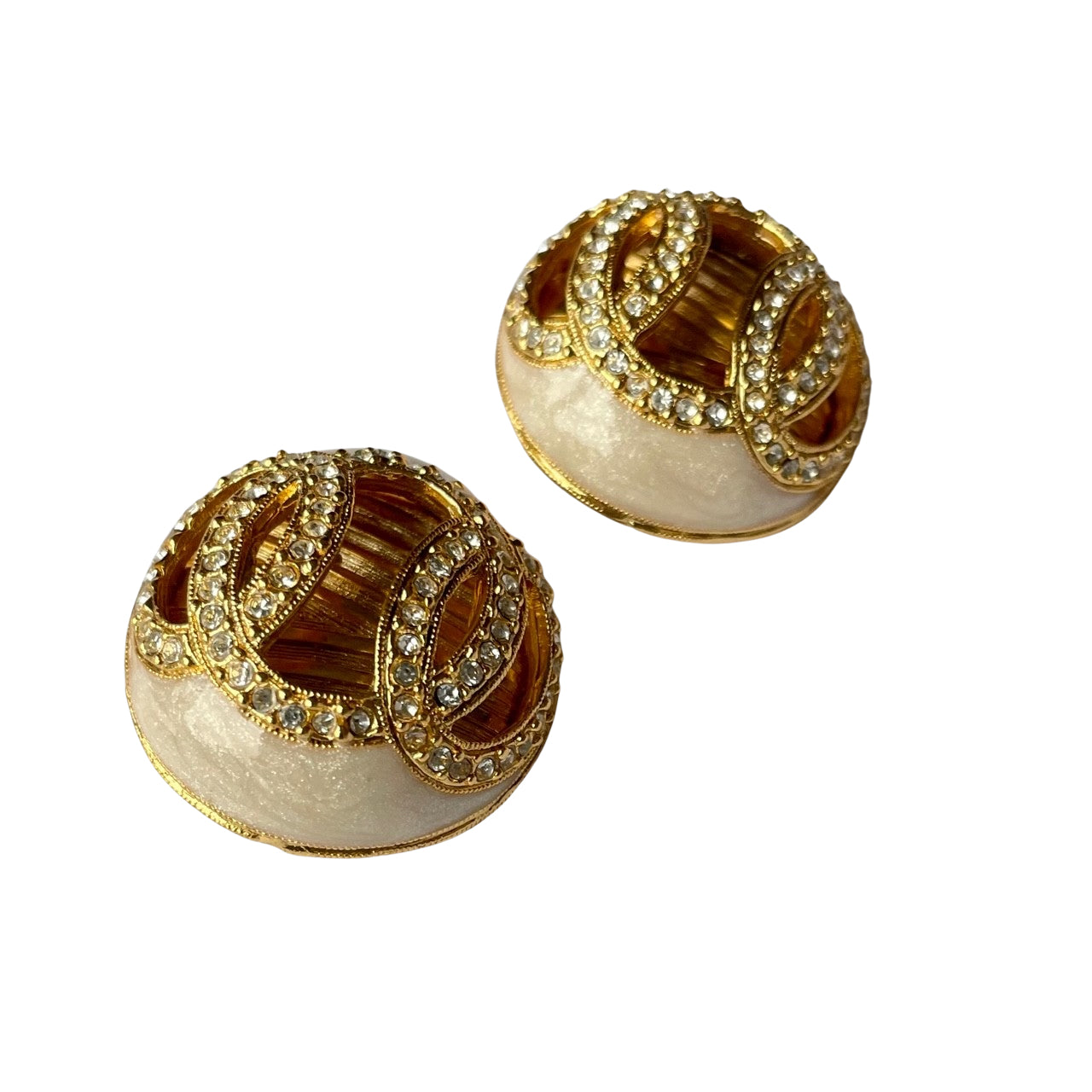 side view of a pair of vintage 1980s Helena Rubinstein Paris domed clip-on earrings. Each button-style earring features a smooth, cream-colored faux pearl base overlaid with intricate gold-tone fluting and two interlocking circular motifs encrusted with small, glittering clear rhinestones.