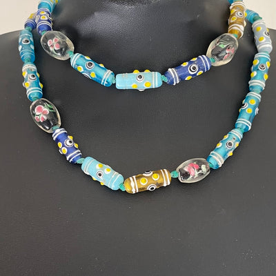 Antique Venetian glass African trade bead necklace in turquoise and blue with eye beads, wedding cake beads and encased floral lampwork beads shown doubled on bust