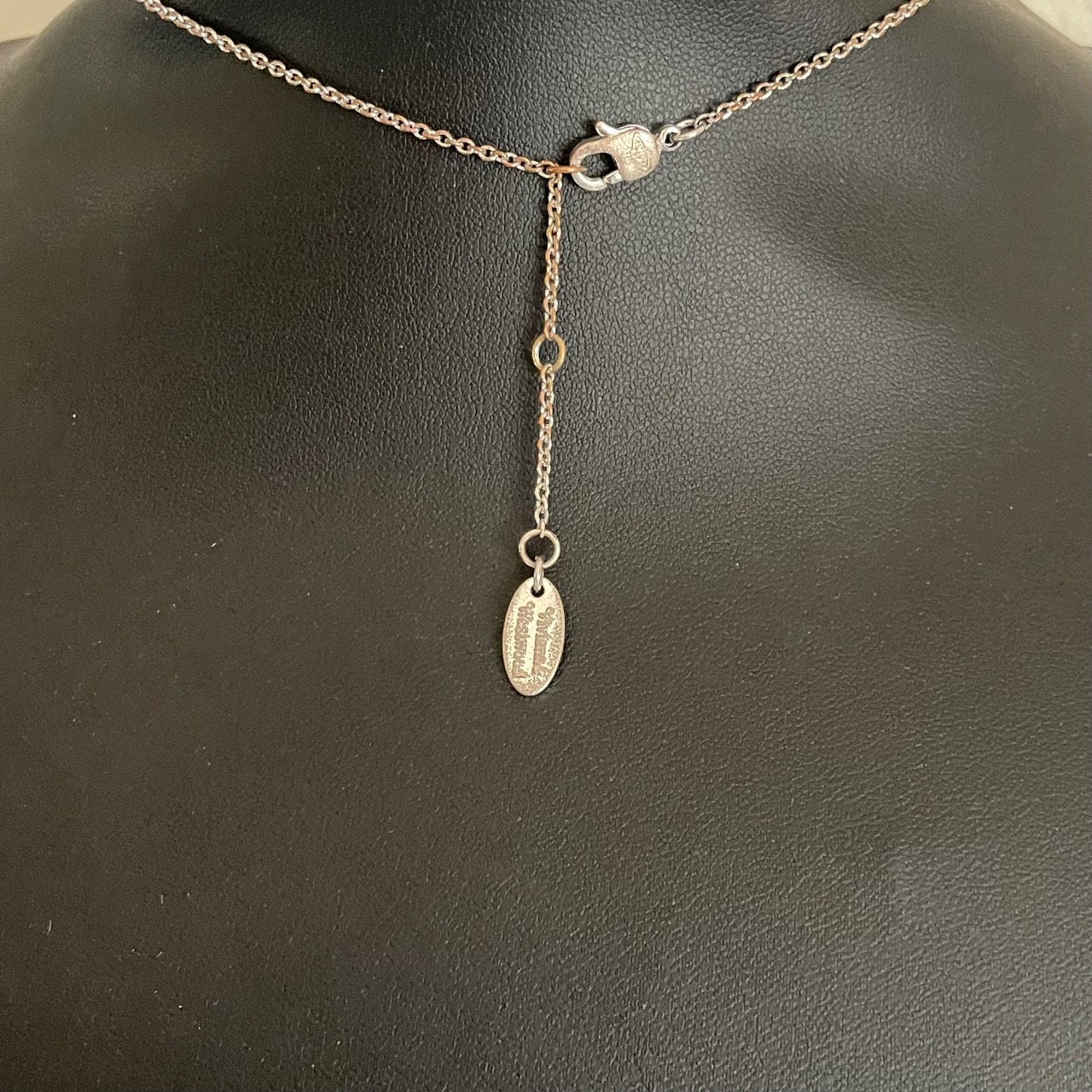 the lobster clasp and extender chain of  silver-tone Vivienne Westwood crystal-encrusted mini orb pendant necklace displayed on a black background.