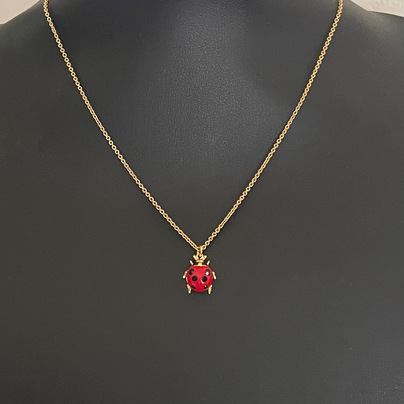 Close-up of a Vivienne Westwood ladybird necklace in gold-tone, featuring a red enamel body with black crystals, dangling orb charm, and hallmark tag.