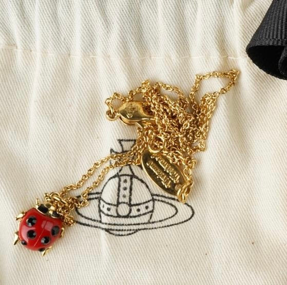 Close-up of a Vivienne Westwood ladybird necklace in gold-tone, featuring a red enamel body with black crystals, dangling orb charm, and hallmark tag.