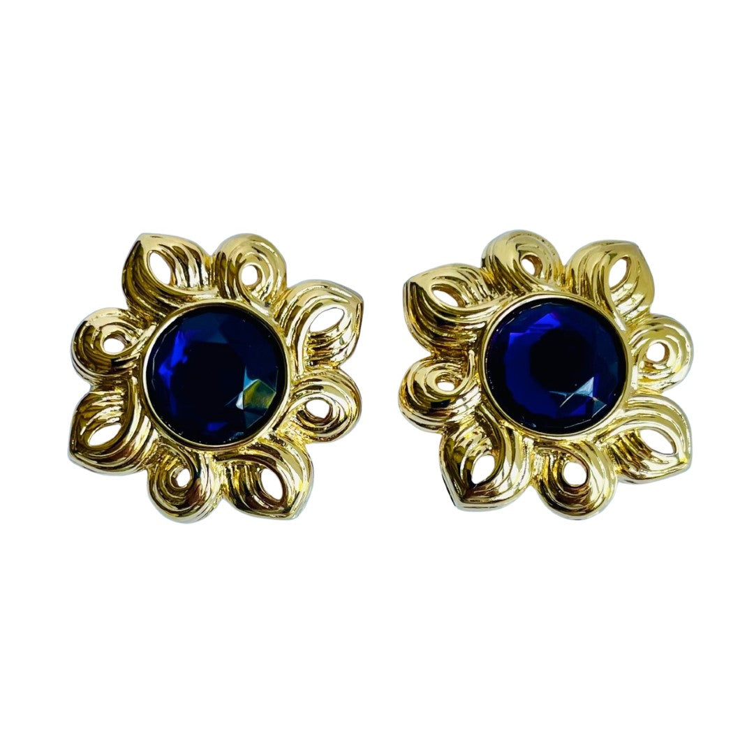 Close-up of a vintage Kenneth Jay Lane sunburst stud earring featuring a deep amethyst purple faceted crystal center, surrounded by a radiating, textured gold-tone openwork ray design.