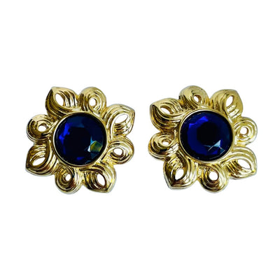 Close-up of a vintage Kenneth Jay Lane sunburst stud earring featuring a deep amethyst purple faceted crystal center, surrounded by a radiating, textured gold-tone openwork ray design.
