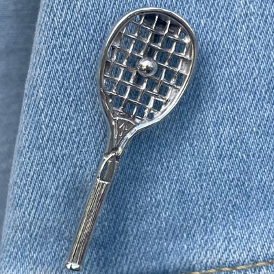 Antique sterling silver tennis racquet brooch on a blue denim background