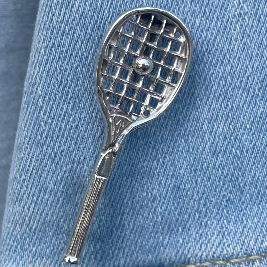 Antique sterling silver tennis racquet brooch on a blue denim background