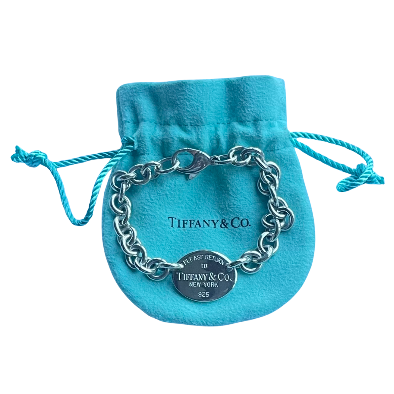 A silver chain bracelet with a clasp and a round signature tag, displayed on a  blue velvet drawstring pouch with 'Tiffany & Co.' printed on it, against a plain white background.