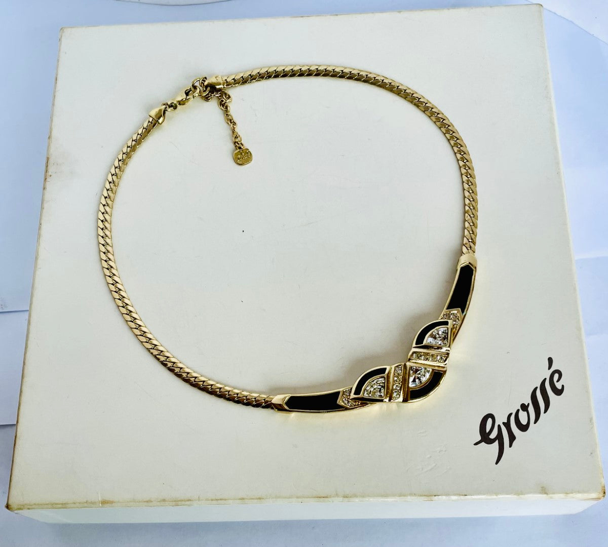 Gold necklace with black accents and gemstones on a 'Grossé' branded box.