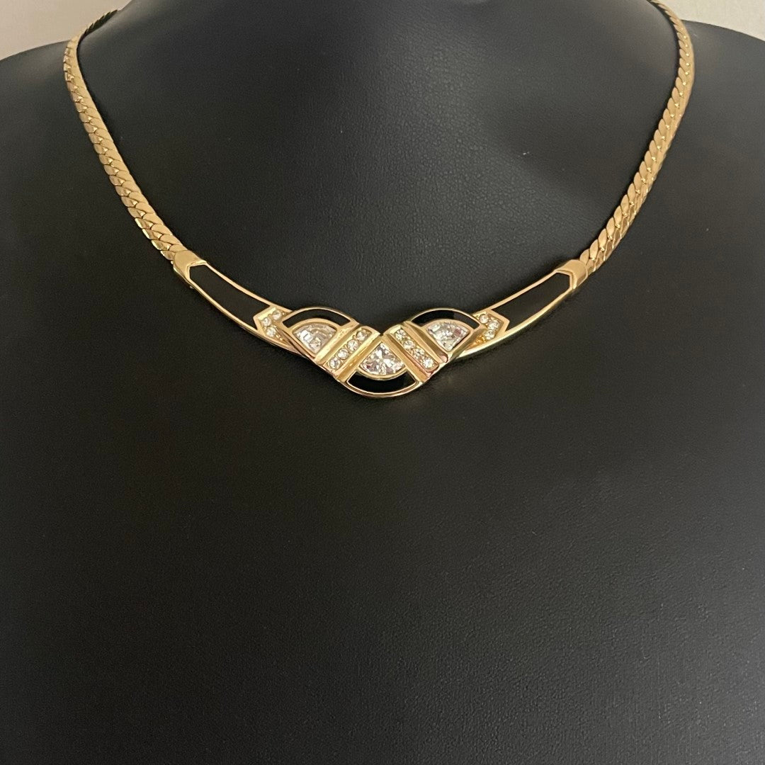 Gold necklace with black accents and gemstones on a black bust.