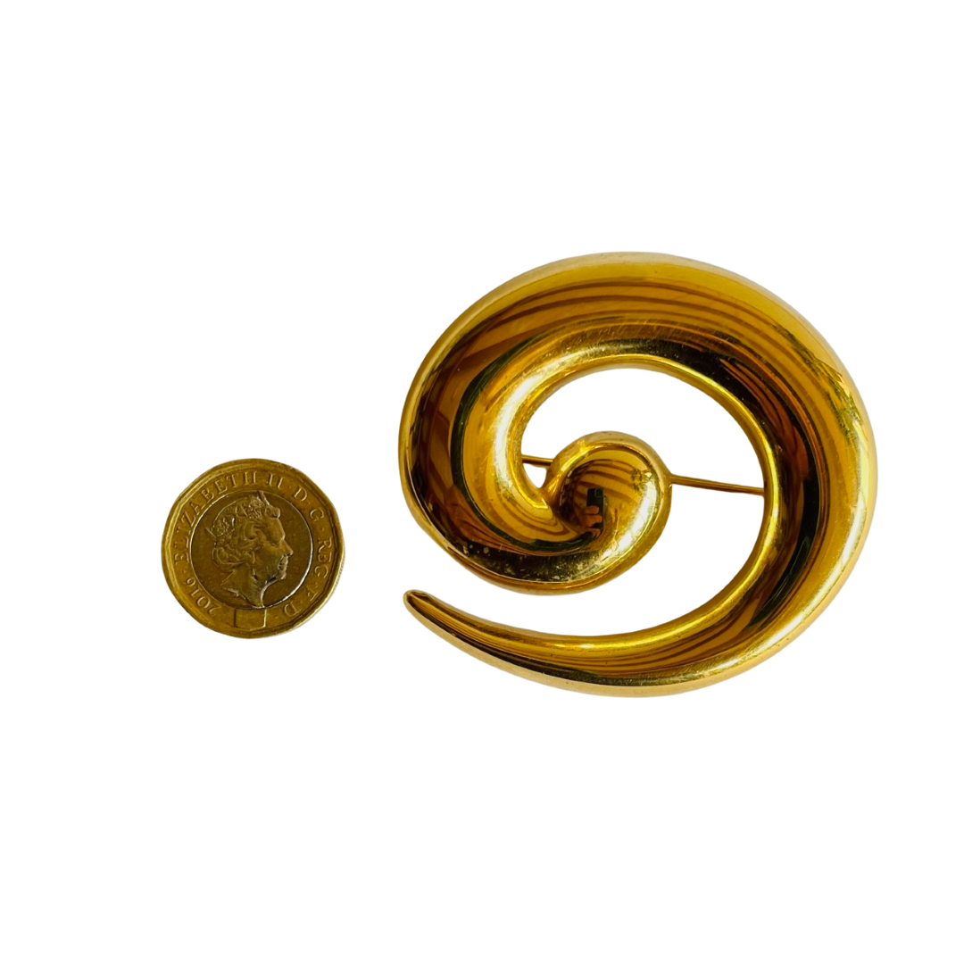reverse of Monet gold plated spiral brooch next to a one pound coin to show scale on a white background