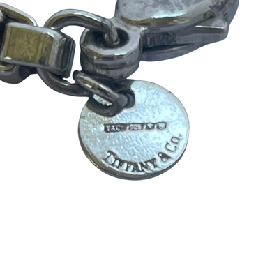 Close-up of a sterling silver bracelet clasp and round Tiffany & Co. logo charm, showing engraved hallmarks and the brand name on a white background.