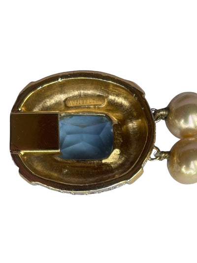 Reverse side of a vintage Vogue Bijoux pearl bracelet clasp, showing the engraved brand signature stamp on a gold-plated setting backing a blue crystal.