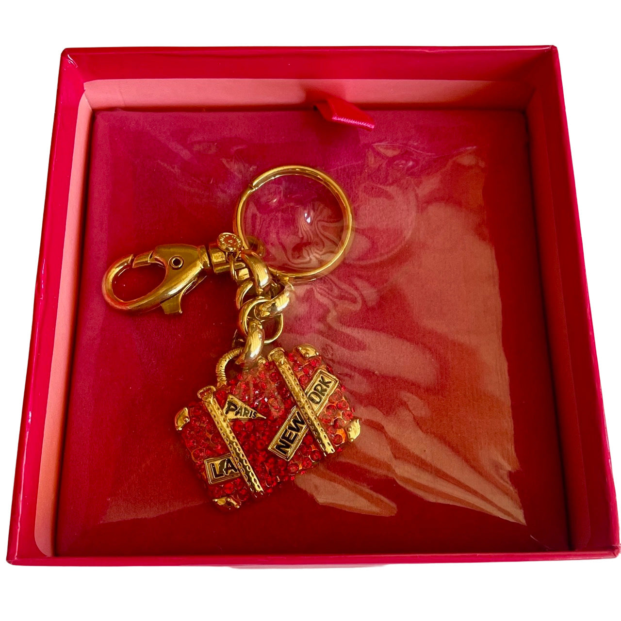 Gold-tone Butler & Wilson suitcase keyring encrusted with red crystals, featuring "Paris," "New York," and "LA" stamps, inside its pink presentation box.