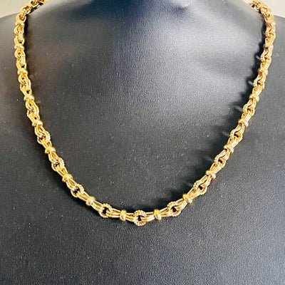 close up of Vintage 1980s Christian Dior matinee length chain necklace in 18ct yellow gold plating, featuring an alternating pattern of stylized figure-of-eight links and textured rope-twist segments, displayed on a black bust