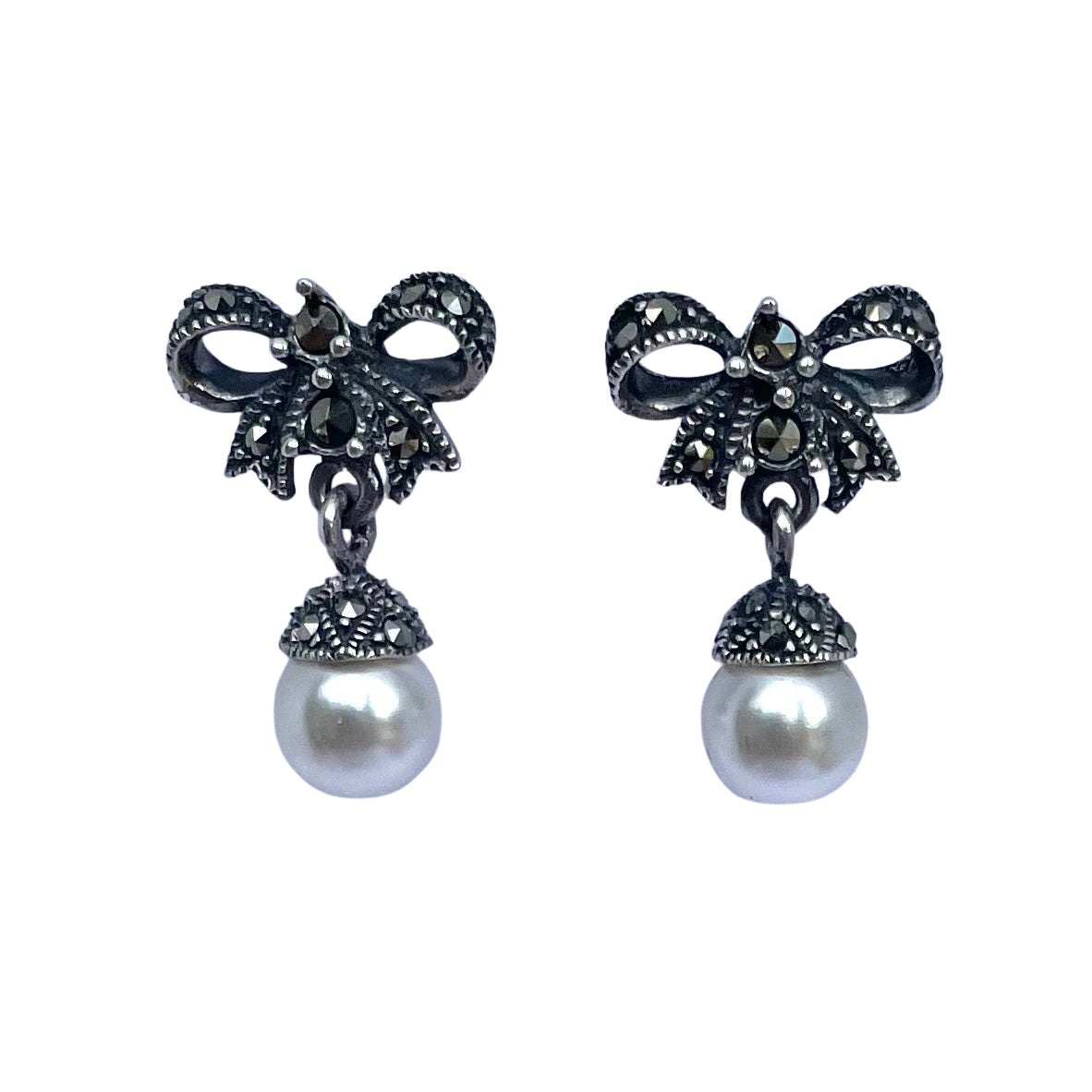 A pair of  925 sterling silver bow-shaped drop earrings embellished with marcasite and finished with a round white pearl hanging below, shown on a plain white background.