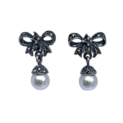 A pair of  925 sterling silver bow-shaped drop earrings embellished with marcasite and finished with a round white pearl hanging below, shown on a plain white background.