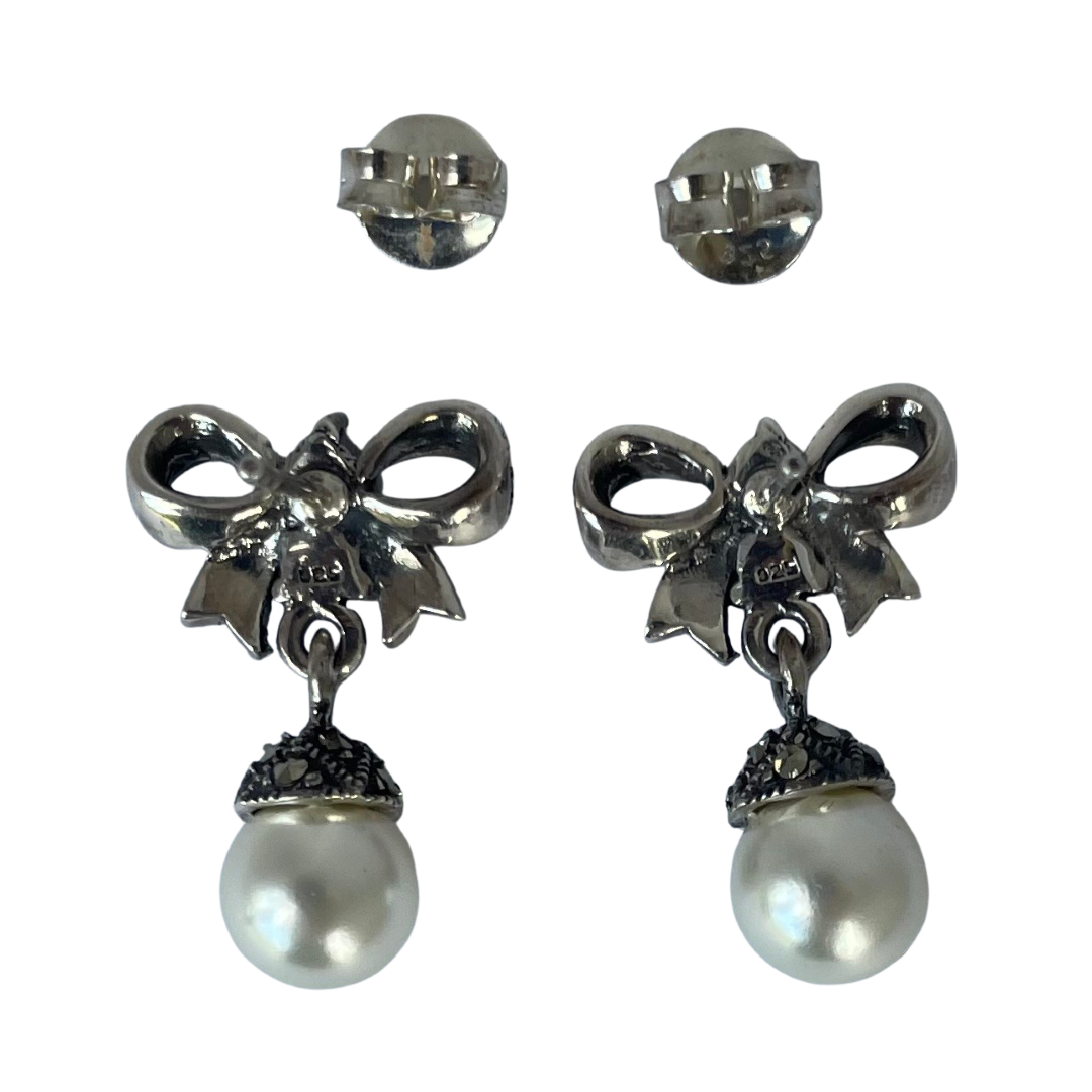 reverse side of a pair of  925 sterling silver bow-shaped drop earrings embellished with marcasite and finished with a round white pearl hanging below, showing the 925 stamp and the butterflies, shown on a plain white background.