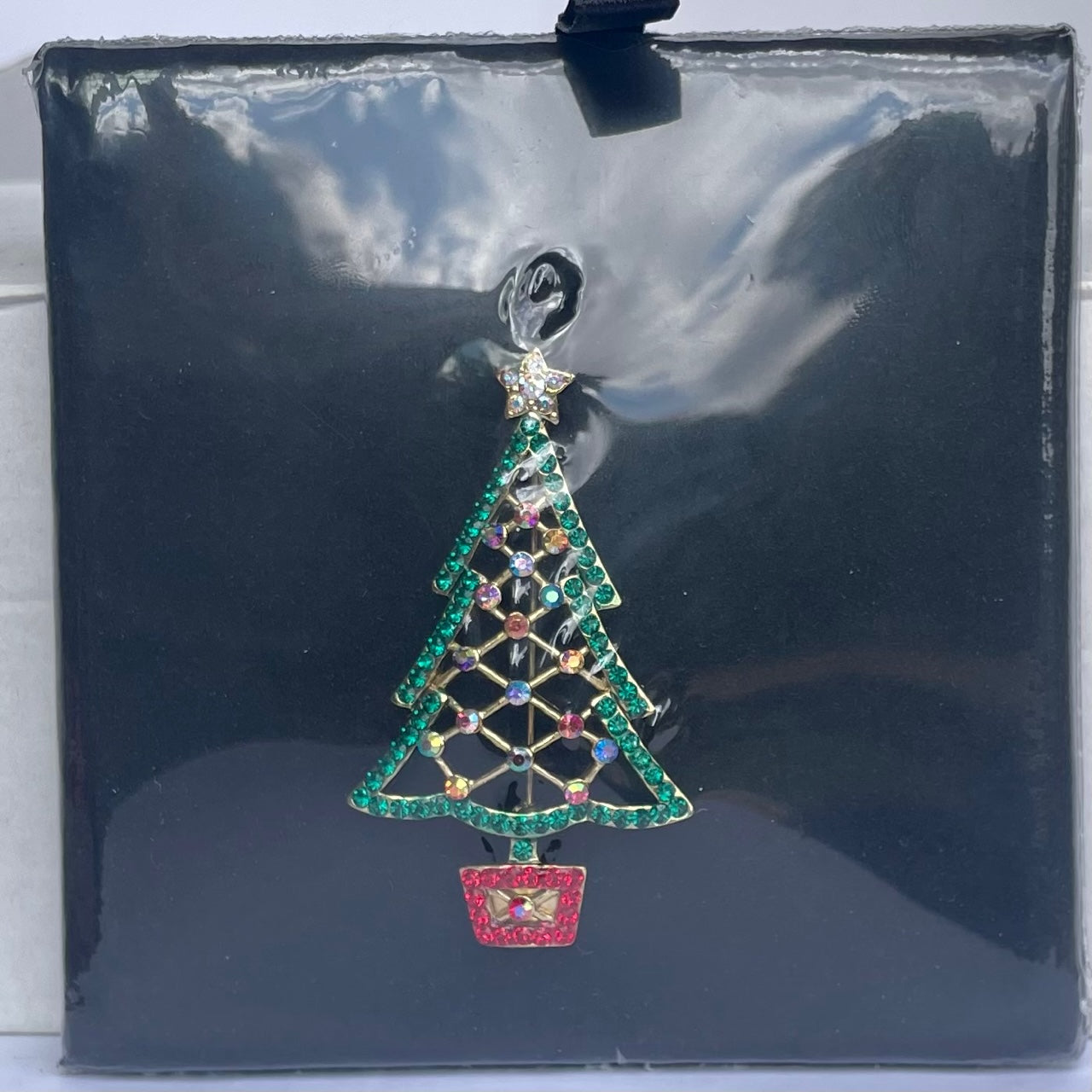 A Butler and Wilson open lattice Christmas tree brooch sett with sparkling green crystals and aurora borealis crystals topped with golden star set with aurora borealis crystals  in pavé set crystal stand displayed in its original cello wrap.