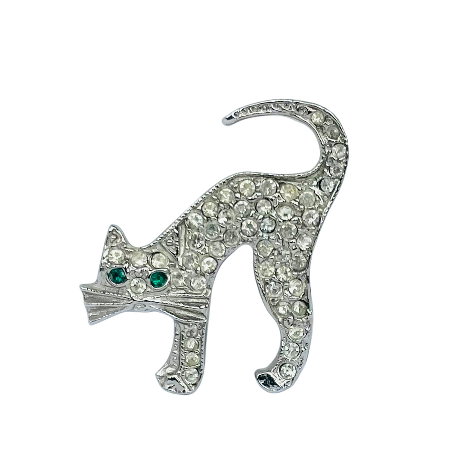 A vintage silver-tone Butler and Wilson arched-back cat brooch completely encrusted with clear pavé rhinestones and featuring two striking emerald green crystal eyes.