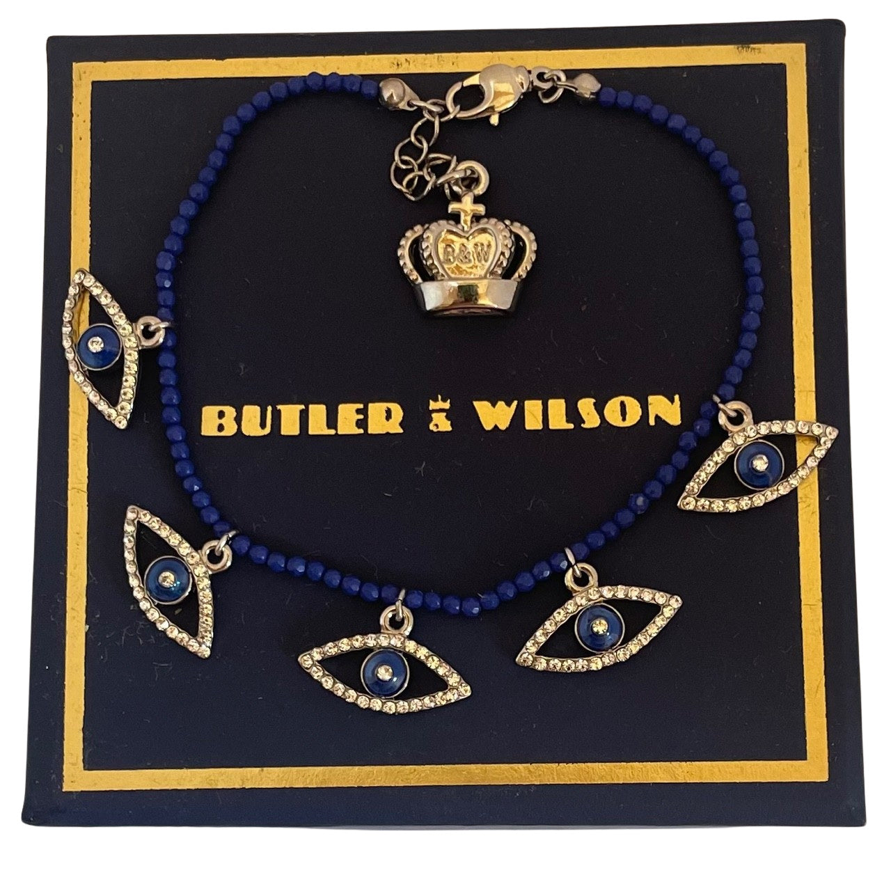 Butler & Wilson crystal eye bracelet with lapis blue beads and crown charm displaying on blue and gold Butler & Wilson box