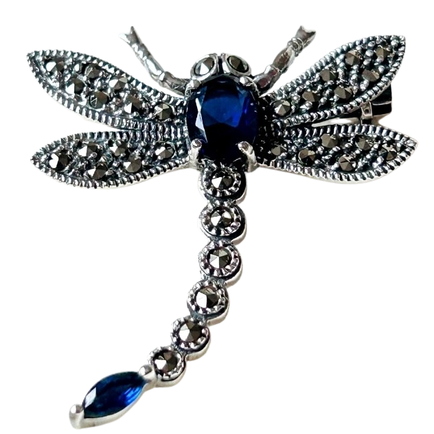 Silver dragonfly brooch with blue gemstones on a white background