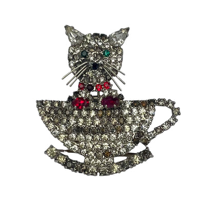Cat-shaped brooch with teacup design and gemstones on a white background
