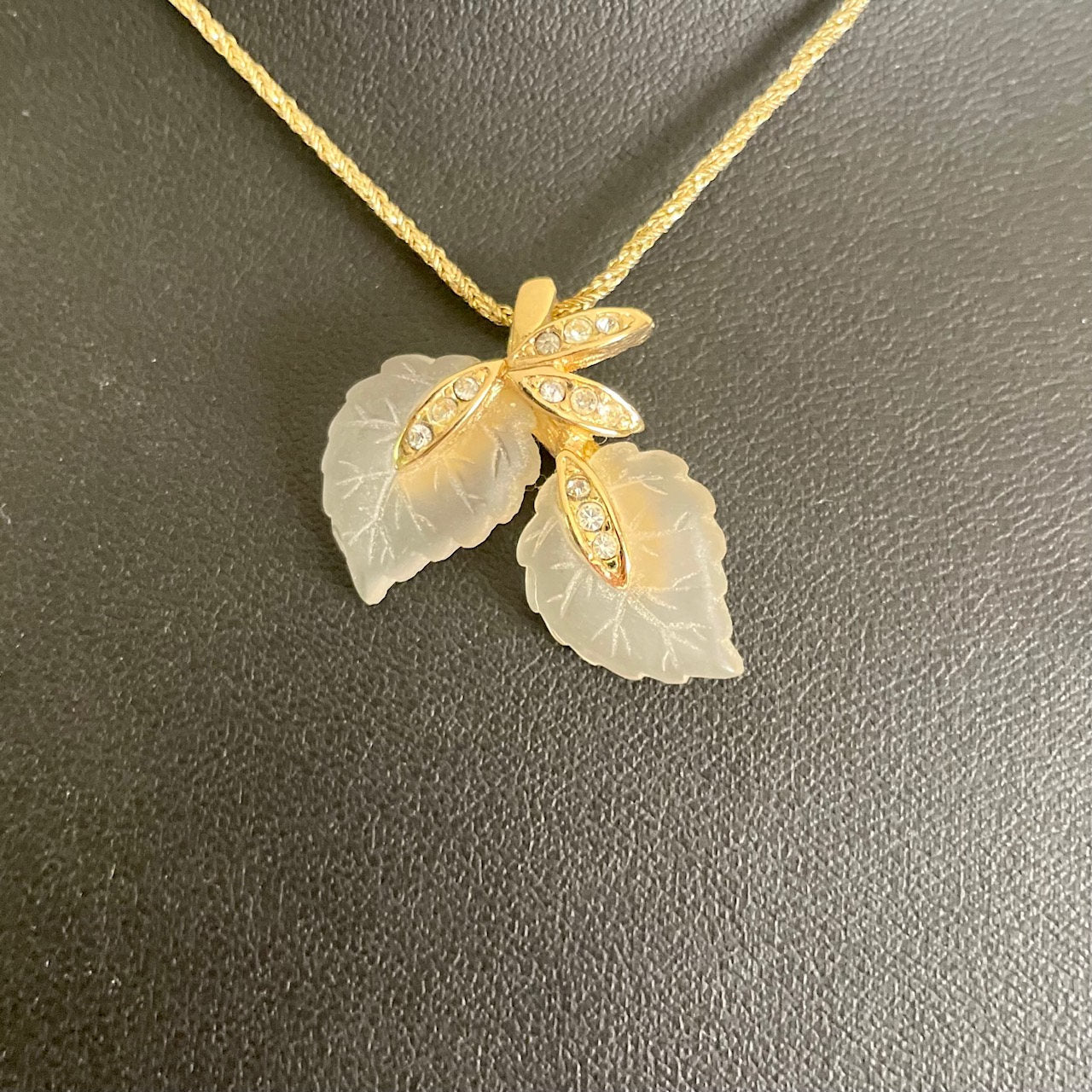 Gold-plated Christian Dior pendant necklace featuring two frosted matte lucite leaves with etched veins, accented by crystal-encrusted gold-toned stems.