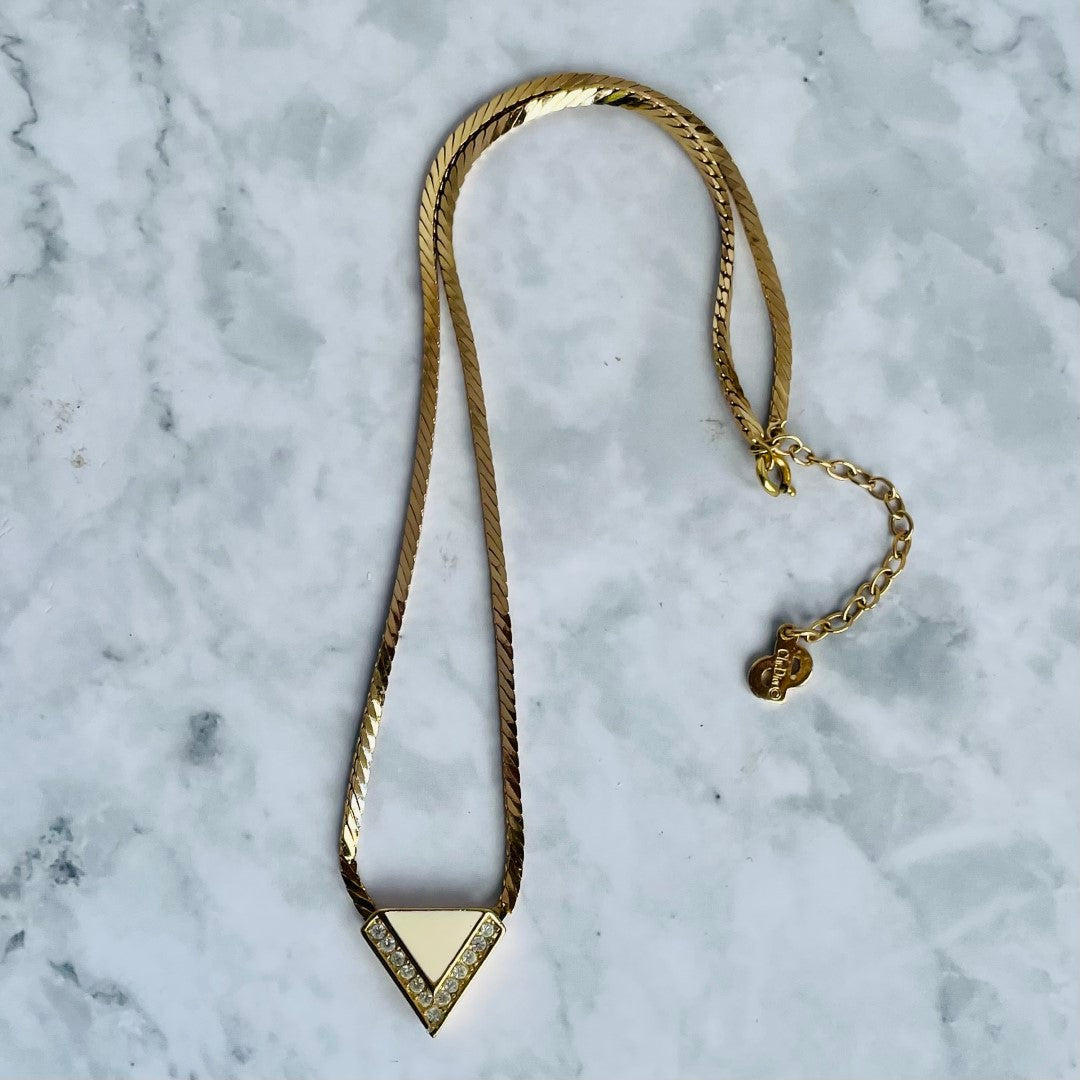 Gold-plated Art Deco style Christian Dior geometric triangle necklace with cream enamel and clear crystal accents on a marble background.