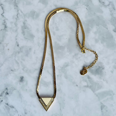 Gold-plated Art Deco style Christian Dior geometric triangle necklace with cream enamel and clear crystal accents on a marble background.