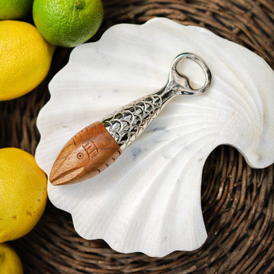 Decorative duo bottle opener with wooden reamer and metal fish design bottle opener shown on a seashell, surrounded by lemons and limes.