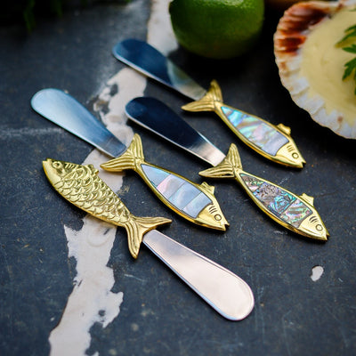 Set of fish-shaped butter knives with mother of pearl handles photographed on a dark surface.