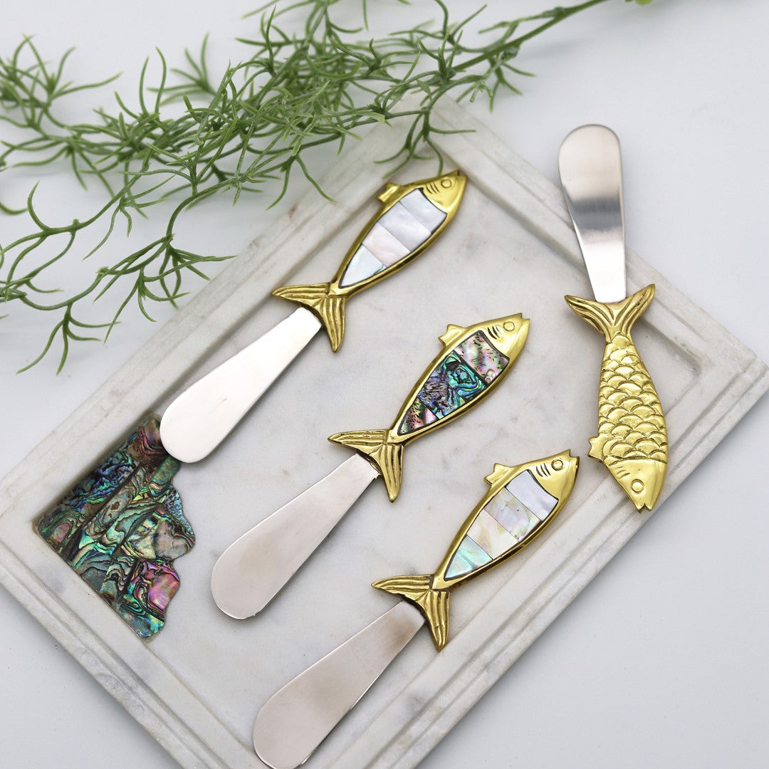 Set of fish-shaped butter knives with mother of pearl handles photographed on a marble tray.