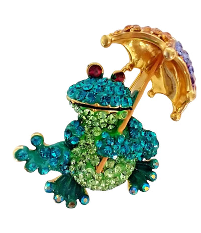 A colourful Butler & Wilson frog-shaped brooch or pin featuring a gold-tone body and umbrella, covered in green and blue rhinestones, with small red rhinestone eyes, on a plain white background.