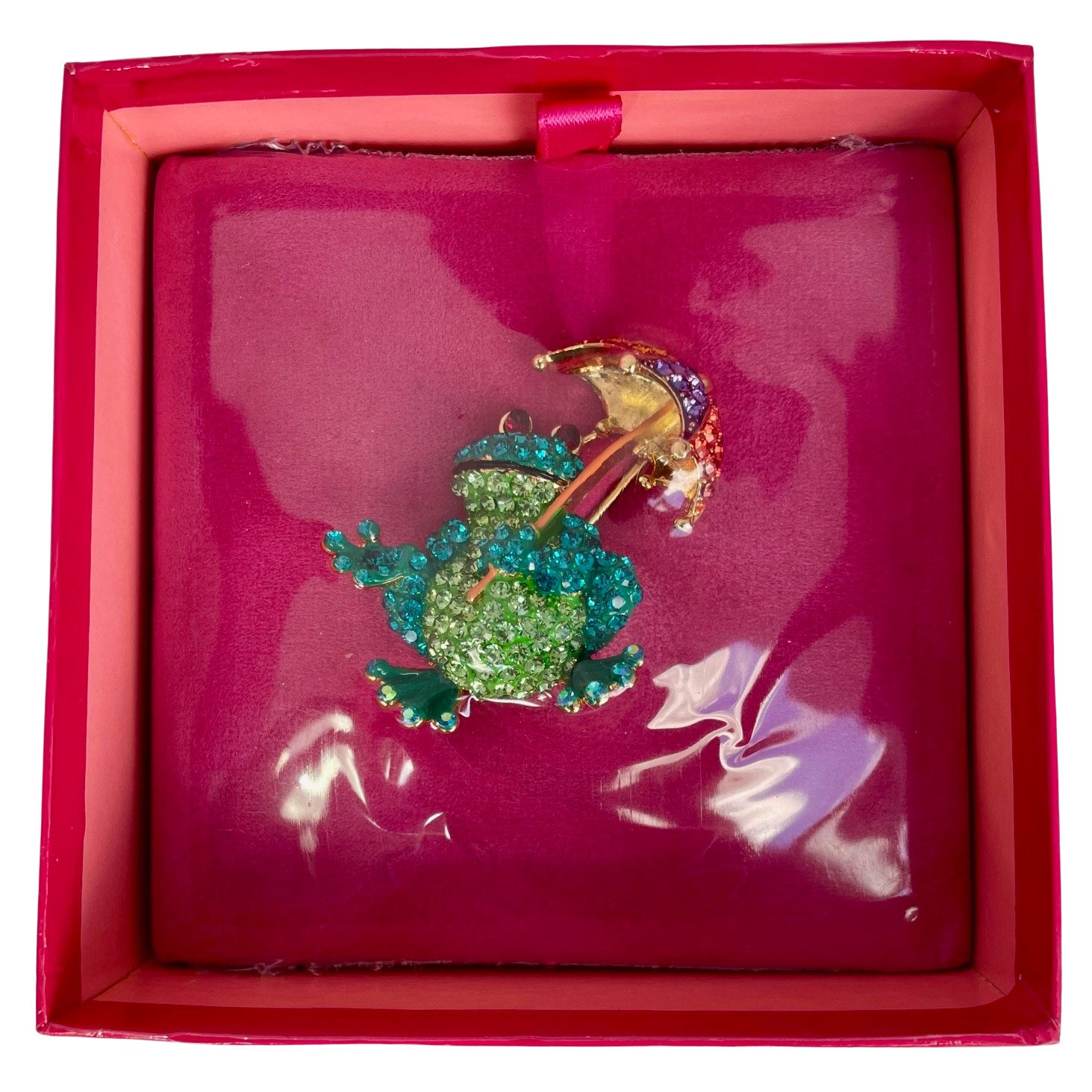 A colourful Butler & Wilson frog-shaped brooch or pin featuring a gold-tone body and umbrella, covered in green and blue rhinestones, with small red rhinestone eyes, on a plain white background still sealed in Butler & Wilson pink box.