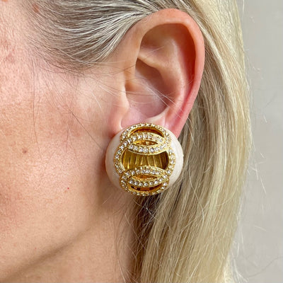 Vintage Helena Rubinstein 1980s earrings shown close up on model. The earrings feature a smooth, cream-coloured pearlescent base emulating mother-of-pearl. They are accented with brilliant, clear crystals, pavé-set in rich gold-plated interlocking circles, overlaid upon a backdrop of textured gold fluting.
