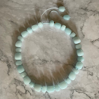 Lola Rose milky-aqua blue quartzite statement necklace with hand-knotted pillow nugget beads and a round yellow-gold-tone charm on an adjustable cord on marble background.