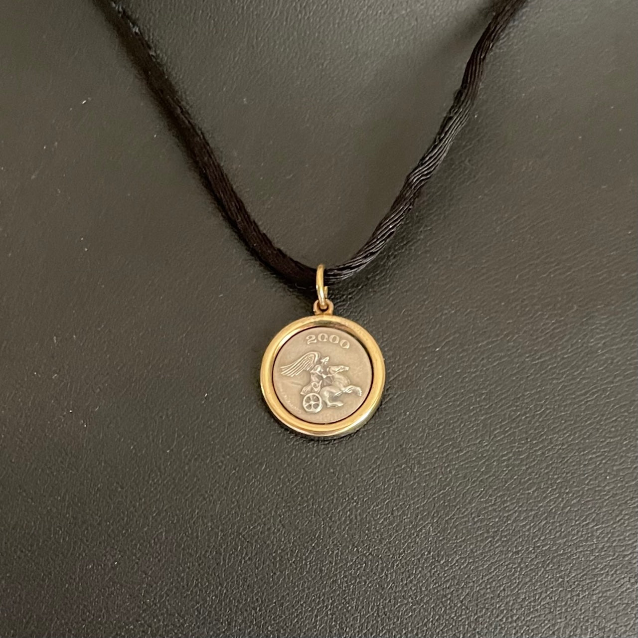 Pristine vintage Ilias Lalaounis necklace showing a 1.6cm 925 sterling silver detailed pendant with an 18K yellow gold border bezel on a 42cm black fabric cord.