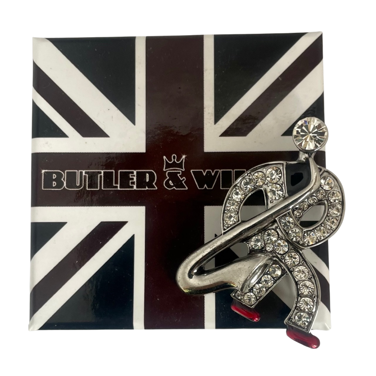 Front view of a silver-tone Butler & Wilson Art Deco style saxophonist brooch against a white background, featuring clear rhinestones and red enamel shoes on signature Butler & Wilson black, white and red box.
