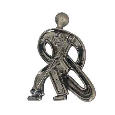 Bacj view of a silver-tone Butler & Wilson Art Deco style saxophonist brooch against a white background, featuring clear rhinestones and red enamel shoes.