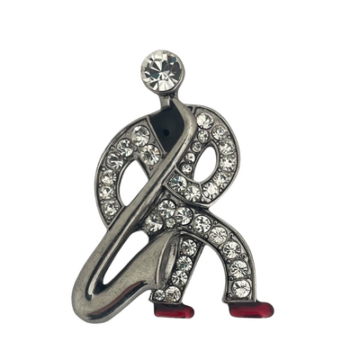 Front view of a silver-tone Butler & Wilson Art Deco style saxophonist brooch against a white background, featuring clear crystals and red enamel shoes.