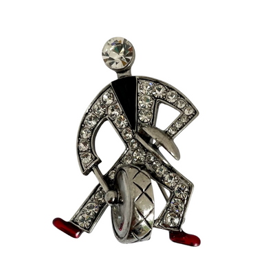 Front view of a silver-tone Butler & Wilson Art Deco style jazz drummer brooch, adorned with clear crystal rhinestones, black enamel, and red enamel shoes