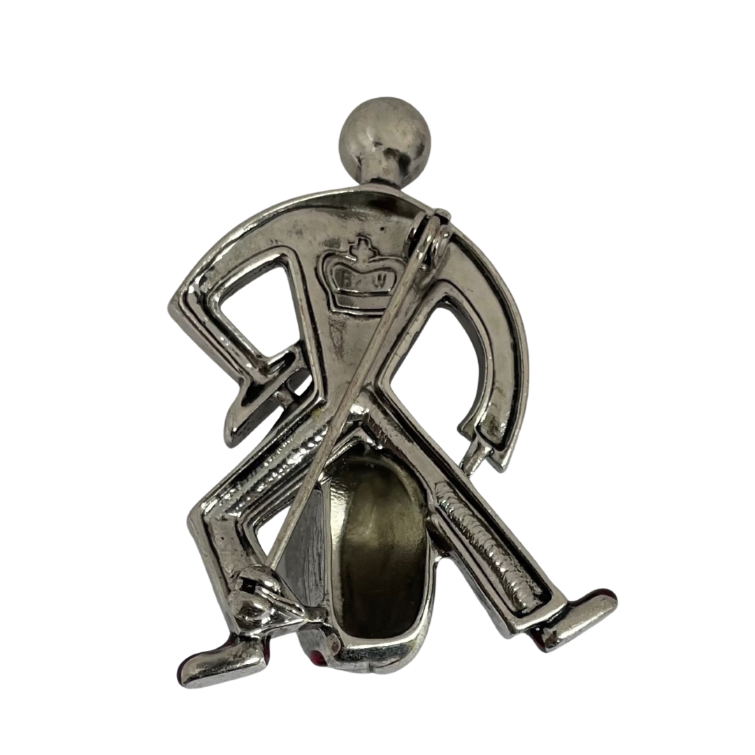 reverse of a silver-tone Butler & Wilson Art Deco style jazz drummer brooch, adorned with clear crystal rhinestones, black enamel, and red enamel shoes. The image shows the Butler & Wilson crown logo and back of pin.
