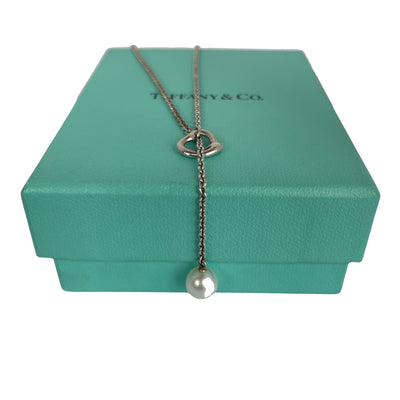 Vintage Tiffany & Co. Elsa Peretti Open Heart sterling silver lariat necklace featuring a sliding open heart pendant and a cultured freshwater pearl on a 19-inch chain, shown in polished pre-owned condition with Tiffany box and pouch.
