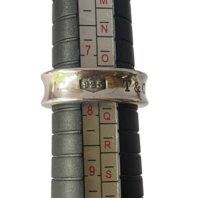 A silver Tiffany & Co. ring being measured on a black metal mandrel ring sizer. The ring sits between sizes 7 and 8, showing the "925" and partial "T & CO" engravings on its outer band.