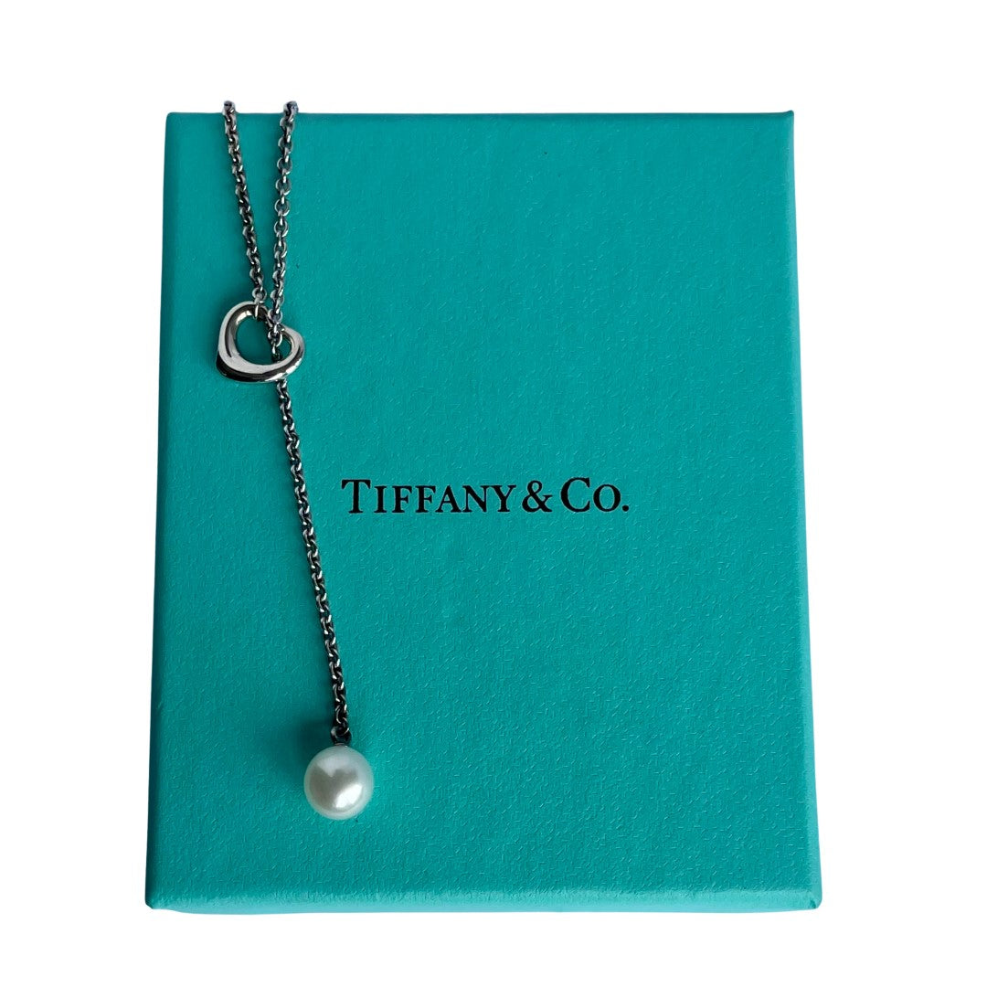 Vintage Tiffany & Co. Elsa Peretti Open Heart sterling silver lariat necklace featuring a sliding open heart pendant and a cultured freshwater pearl on a 19-inch chain, shown in polished pre-owned condition with Tiffany box and pouch.