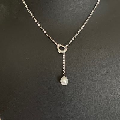 Vintage Tiffany & Co. Elsa Peretti Open Heart sterling silver lariat necklace featuring a sliding open heart pendant and a cultured freshwater pearl on a 19-inch chain, shown in polished pre-owned condition with Tiffany box and pouch.